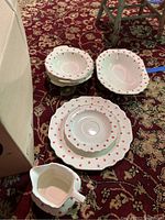 Stacks of Lido dishware including dinner plates, bowls, and a gravy boat featuring red floral pattern on white with gold trim, placed on a patterned red carpet.