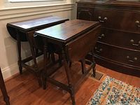 Full view of the pair of wooden drop leaf tables side by side showing their size and structure near a window and rug.