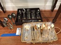 Full view of multiple flatware pieces organized in a wooden tray with additional flatware in a basket wrapped in plastic.