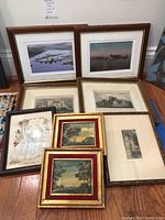 Nine framed art pieces arranged on the floor, including airplane photographs, prints of trees, castle, and fashion figure prints