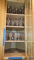Shelved collection of clear stemmed wine glasses and shorter water glasses with decorative cut glass patterns.