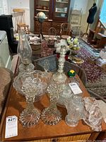 Photo showing various glass items including candleholders, a bowl, a mercury glass candle holder, mini pitchers, and a hurricane lamp.