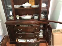 Display cabinet showing china dishes and covered serving dishes with floral pink and purple pattern and gold trim.