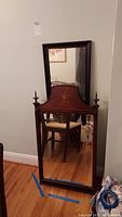 Vintage wooden framed mirror with inlaid wood design at top, finial finials, and scratch marks, reflecting room furniture.