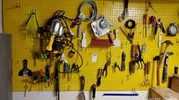 Wide view of various tools, electric lights, and safety goggles hung on yellow pegboard
