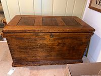 Front view of aged wooden carpenter's trunk with key lock and visible scratches.