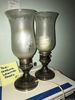 Pair of weighted sterling lamp bases with frosted glass shades showing etched grape and leaf patterns placed on a surface.