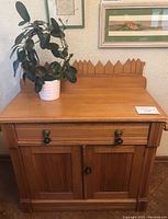 Front view of antique pine washstand with a plant on top, showing drawer and doors and decorative raised back