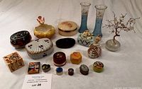 Overview of all lots showing assortment of tins, dishes, vases, and figurines arranged on a white surface.