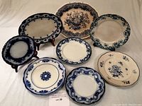 Set of 8 blue and white plates and platters arranged on table with some on stands, showing various floral and border designs in blue on white.