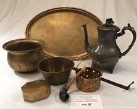 Full set of brass items arranged together showing platter, bowl, tin, basket, teapot, pipe and metal rod
