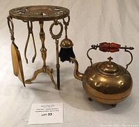 Brass fireplace tool set on stand next to brass teapot