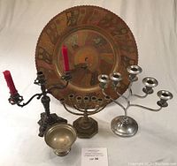 Two ornate metal candlesticks, one menorah, one metal goblet, and large decorative tray arranged on table