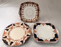 Three decorative dinner plates placed on a flat surface showing floral and geometric patterns in orange, blue, brown and red with various shapes including square and round.