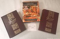 Three collectible cookbooks displayed together including two volumes of The Gourmet Cookbook in brown covers and one copy of Larousse Gastronomique with dust jacket