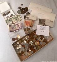 Overview of assorted foreign bills and coins spread on a cloth surface, including envelopes marked Spanish, Polynesia, Austria, and Swiss.