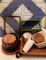 Framed quilt in blue and white geometric pattern with assorted baskets and green metal shelf in front.
