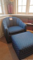 Navy upholstered armchair with curved back and arms, situated next to a bookshelf and window. The chair has small white pattern throughout the fabric and is on casters.