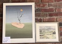 Framed surrealist style painting by B. Wheeler depicting a small boat with a flower, shown next to the smaller framed landscape by D. Graveling.