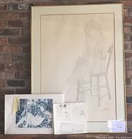 Main framed pencil drawing of seated nude woman next to smaller prints/sketches taped on backing.