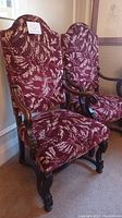 Full side angle view of two high-backed chairs showing velvet upholstery and carved wooden arms and legs with scroll detail.