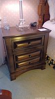 Front view of one dark wood bedside table showing two drawers with round knobs and decorative recessed panel detail on drawer fronts.