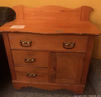 Front view of pine wood cabinet with three drawers and one door, showcasing brass drawer handles and a knob on the door.
