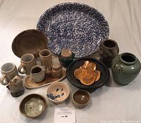 Overall view of the pottery lot showing platter, vases, mugs, pitchers, bowls, jar with lid, and coasters