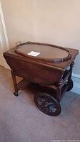 Tea cart closed with glass tray on top, showing drop leaves folded down and large wheels on one side.