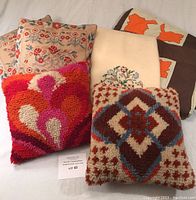 Photo showing double size hand embroidered wool quilt and five throw pillows: two needlepoint floral, one pink-red fluffy, one rugged wool geometric, and one with orange animal motifs