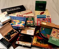 Wide view of multiple vintage boxed board games stacked including Clue, Monopoly, Pictionary, Memory, Snakes and Ladders, Pass the Pigs and chess set in wooden box.