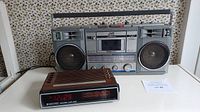 Full view of the JVC vintage boom box radio cassette recorder next to the Baycrest electronic clock radio showing front and controls.