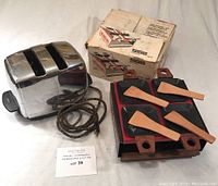 Full view of the 2-slice stainless steel toaster with power cord and original box, alongside the raclette set pans and wooden spatulas.