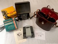 Photo of the black Super 8 viewer with fold-out screen, Hanimex Universal 8 splicer box, and Boss binoculars in leather case.