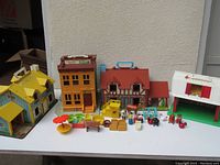 Wide view of all Fisher Price playhouses and accessories arranged on table, showing playsets and numerous small figures and furniture pieces.
