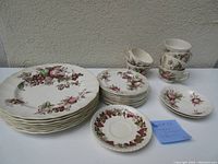 Full set of Johnson Brothers china pieces arranged on a table showing 6 teacups, 7 dinner plates, several saucers, and small plates with brown-red fruit and leaf designs on white ceramic.
