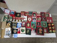 Wide view of 38 assorted vintage Christmas ornaments on table, many in original boxes, including sets and single pieces from Waterford, Lenox, Enesco, International Silver Company, Villeroy & Boch.