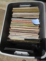 Top view of a large plastic bin filled with approximately 95 vinyl records, showing a tightly packed assortment of album covers and record sleeves.