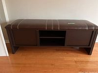 Front view of the brown leather top wood frame bench with storage compartments underneath.