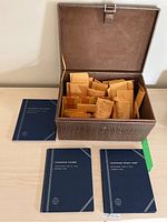 Opened faux leather textured box containing multiple labeled envelopes holding Canadian coins, alongside three blue Whitman albums for Canadian coin collections.