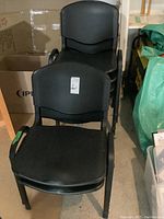 Six black Flexon chairs stacked partially and arranged in pairs, showing metal frames and vinyl surfaces clearly.