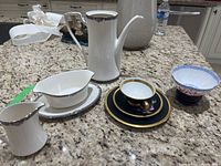 View of all china items including the Noritake bowl, Carlsbad plates, teapot, creamer, sauce boat, tea cup and decorative bowl on granite countertop.