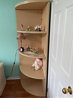 Corner shelving unit with curved shelves holding small decorative figurines and ornaments, showing its shape and shelf spacing to illustrate storage capacity and condition.
