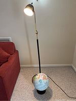 Full view of the black and brass floor lamp with the globe placed on the carpet beside it.
