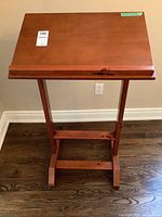 Front view of the stained maple lectern showing flat angled top surface, central support post, and base with crossbars on dark wood floor.
