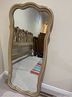 Front view of wood framed mirror showing scalloped edges and light wood color with reflection of adjacent furniture.
