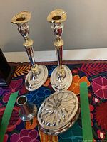 Two silver plate candle holders, silver plate covered container, and multi-color embroidered runner visible