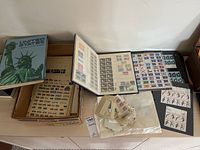 Full view of several stamp albums and loose sheets laid out on a table showing various stamps and packaging.
