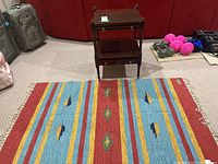 View of the table on wheels with small drawer and the rug underneath, showing the size and condition of both items.
