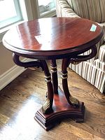 Photo showing the full round tabletop, carved legs, and triangular base with gold accents.